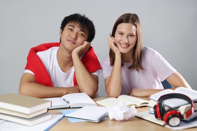 Photo of Happy students with books preparing for exam at table near grey wall