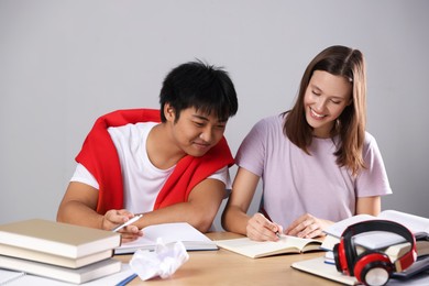 Photo of Happy students with books preparing for exam at table near grey wall