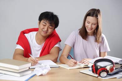 Photo of Happy students with books preparing for exam at table near grey wall