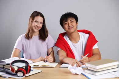 Photo of Happy students with books preparing for exam at table near grey wall
