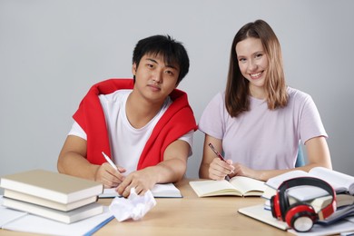 Photo of Students with books preparing for exam at table near grey wall