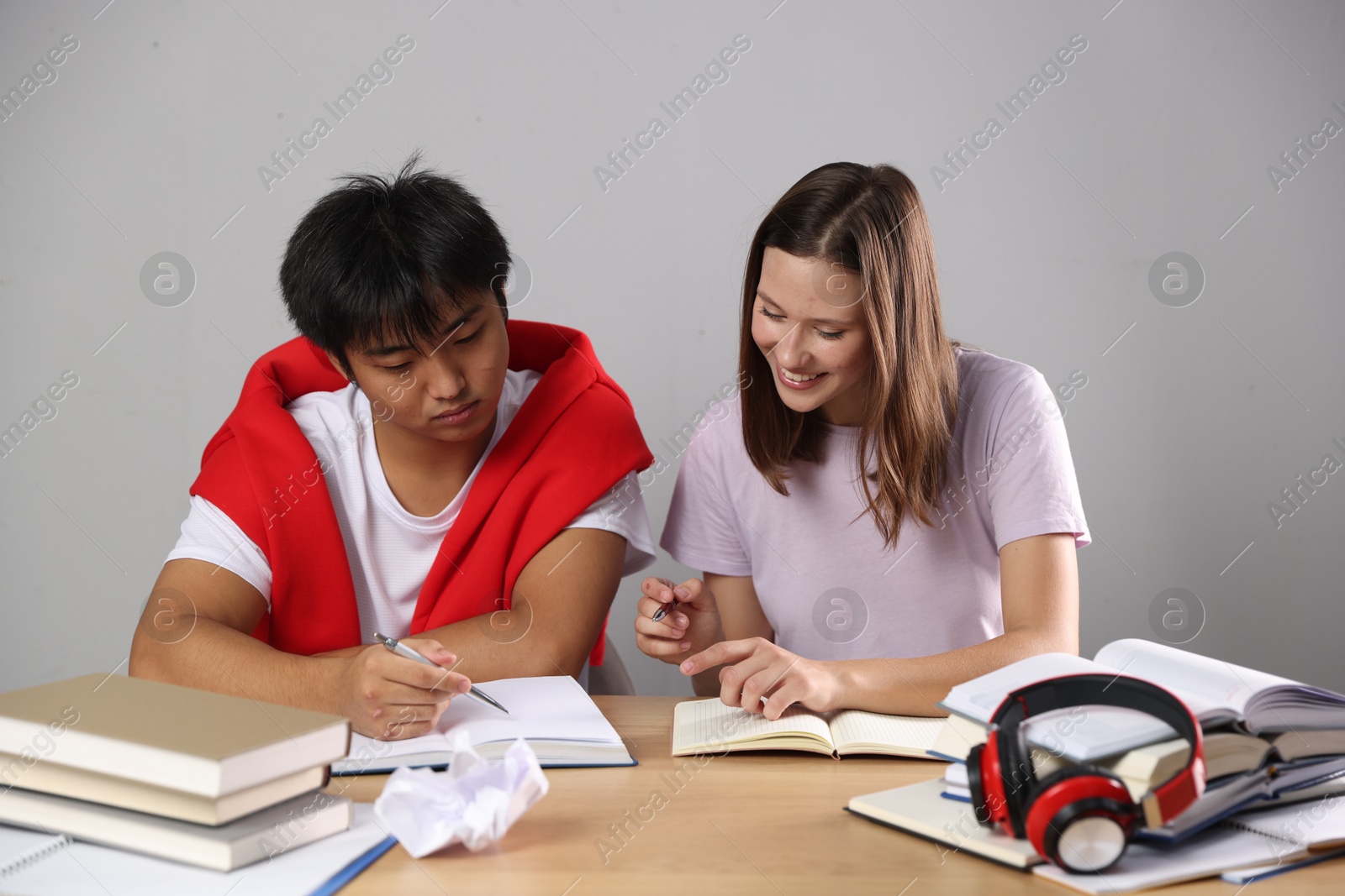 Photo of Students with books preparing for exam at table near grey wall
