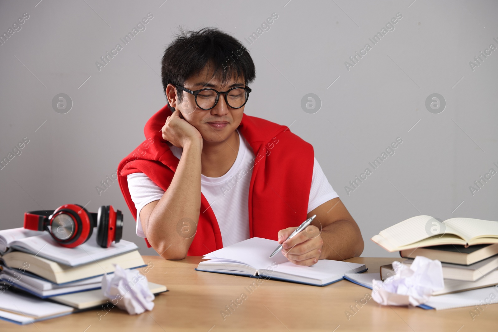 Photo of Student with pen and books preparing for exam at wooden table near grey wall
