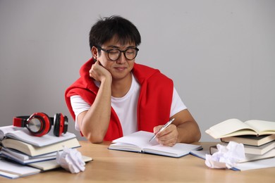 Photo of Student with pen and books preparing for exam at wooden table near grey wall