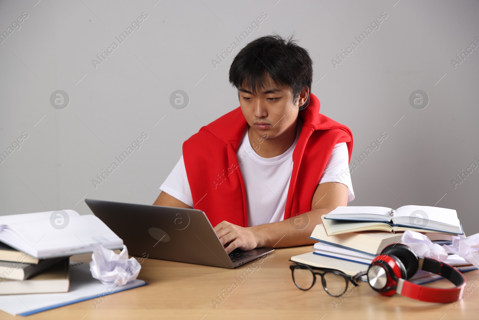 Photo of Student with laptop and books preparing for exam at wooden table near grey wall