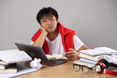 Photo of Student with laptop and books preparing for exam at wooden table near grey wall
