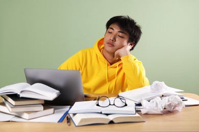 Photo of Student with laptop and books preparing for exam at wooden table near green wall