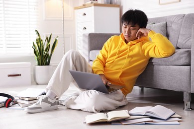 Photo of Student with laptop and books preparing for exam on floor at home