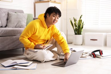 Photo of Student with laptop and books preparing for exam on floor at home