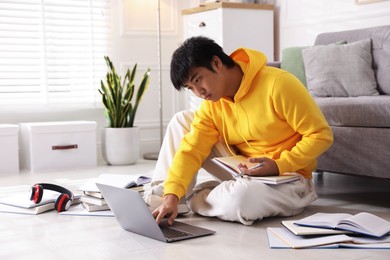 Photo of Student with laptop and books preparing for exam on floor at home