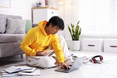 Photo of Student with laptop and books preparing for exam on floor at home
