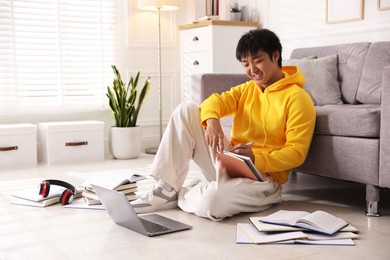 Photo of Smiling student with laptop and books preparing for exam on floor at home. Space for text