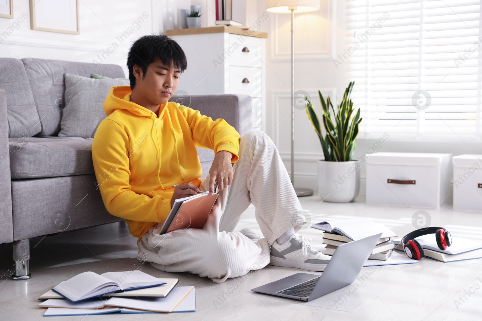 Photo of Student with laptop and books preparing for exam on floor at home