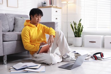 Photo of Student with laptop and books preparing for exam on floor at home