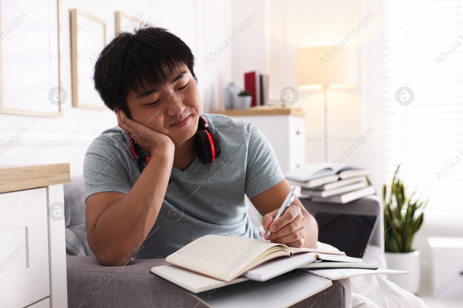 Photo of Student with pen and books preparing for exam on sofa at home