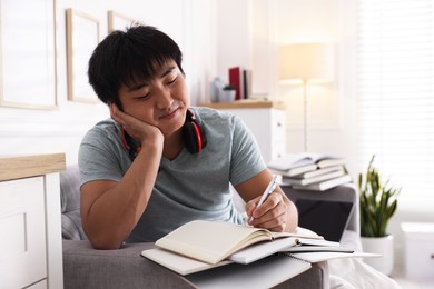 Photo of Student with pen and books preparing for exam on sofa at home