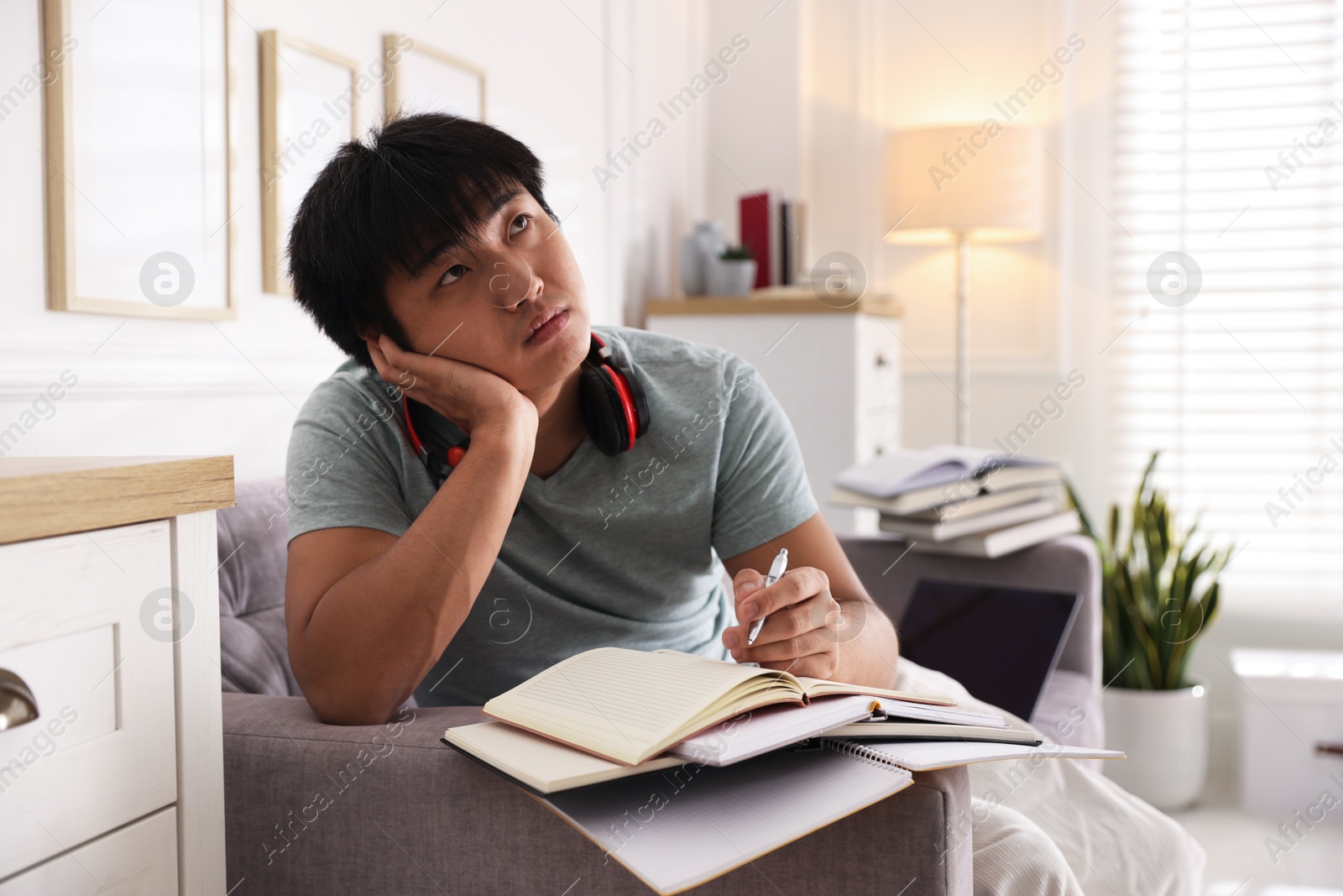 Photo of Student with pen and books preparing for exam on sofa at home