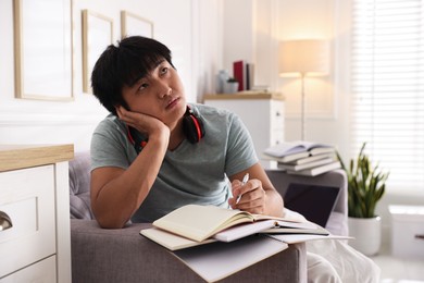Photo of Student with pen and books preparing for exam on sofa at home
