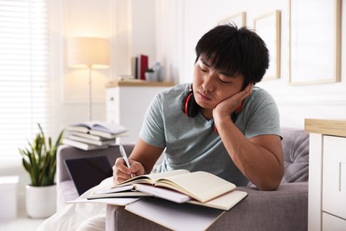 Photo of Student with pen and books preparing for exam on sofa at home