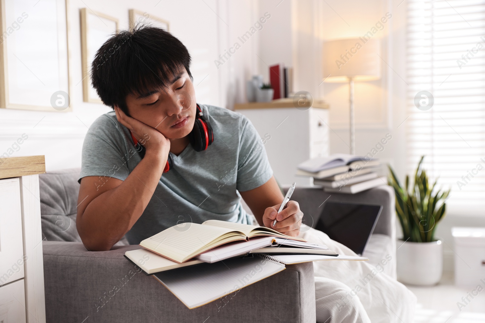 Photo of Student with pen and books preparing for exam on sofa at home