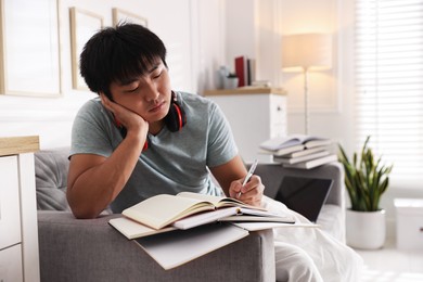 Photo of Student with pen and books preparing for exam on sofa at home