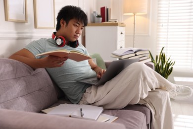 Photo of Student with laptop and books preparing for exam on sofa at home