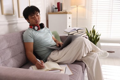 Photo of Student with laptop, pen and books preparing for exam on sofa at home