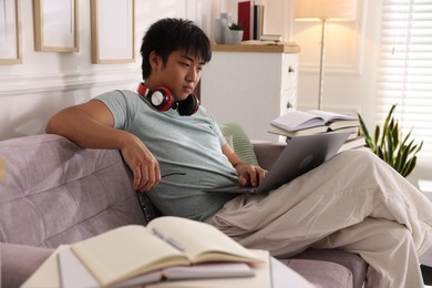 Photo of Student with laptop and books preparing for exam on sofa at home