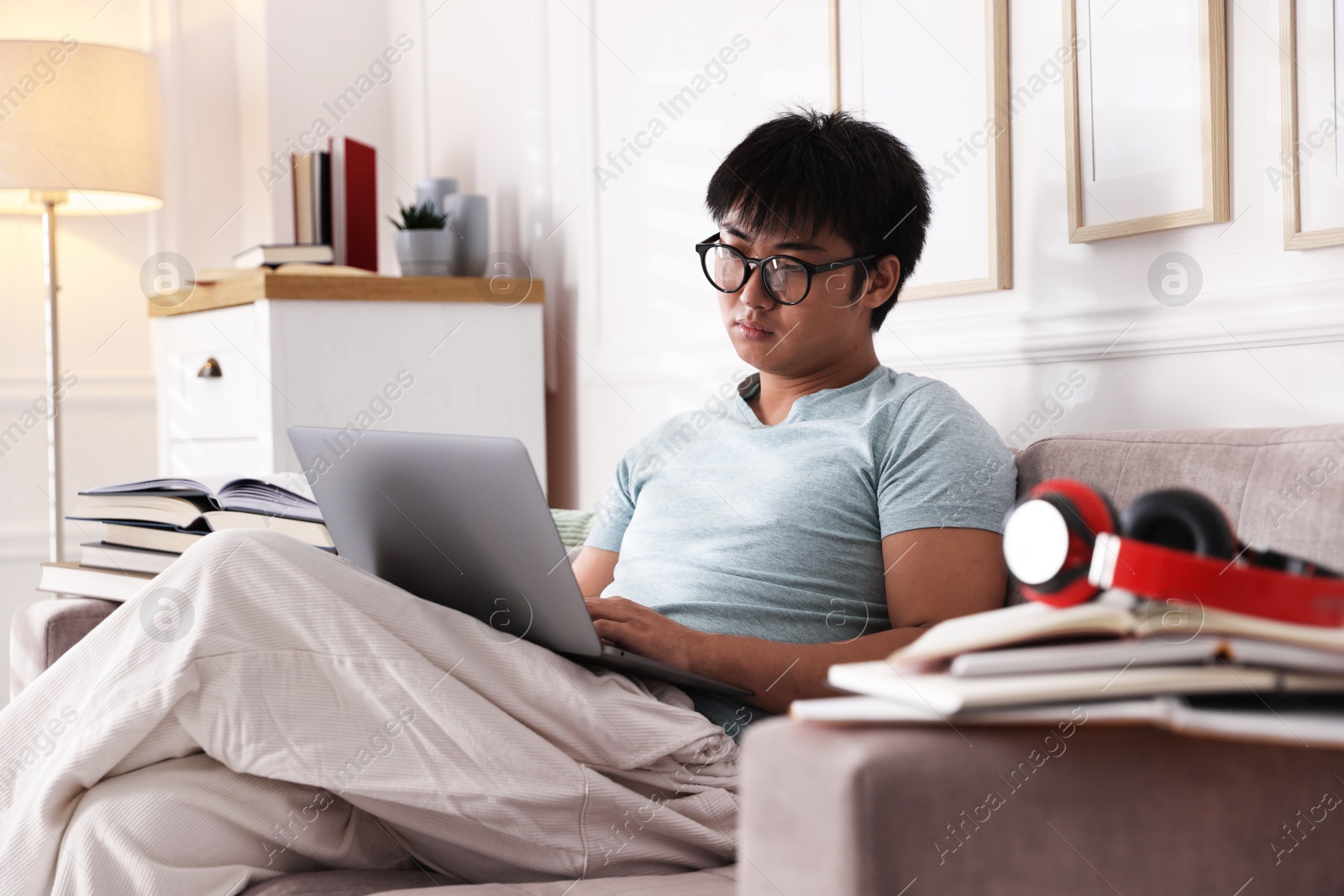 Photo of Student in glasses with laptop and books preparing for exam on sofa at home