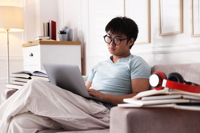 Photo of Student in glasses with laptop and books preparing for exam on sofa at home
