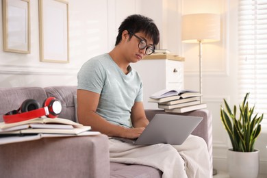 Photo of Student in glasses with laptop and books preparing for exam on sofa at home
