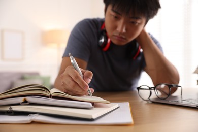 Photo of Student with pen and books preparing for exam at table indoors, selective focus