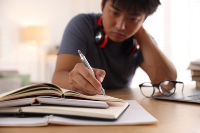 Photo of Student with pen and books preparing for exam at table indoors, selective focus