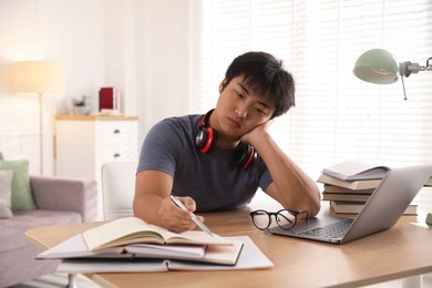 Photo of Student with laptop and books preparing for exam at table indoors
