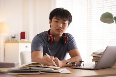 Photo of Student with laptop and books preparing for exam at table indoors