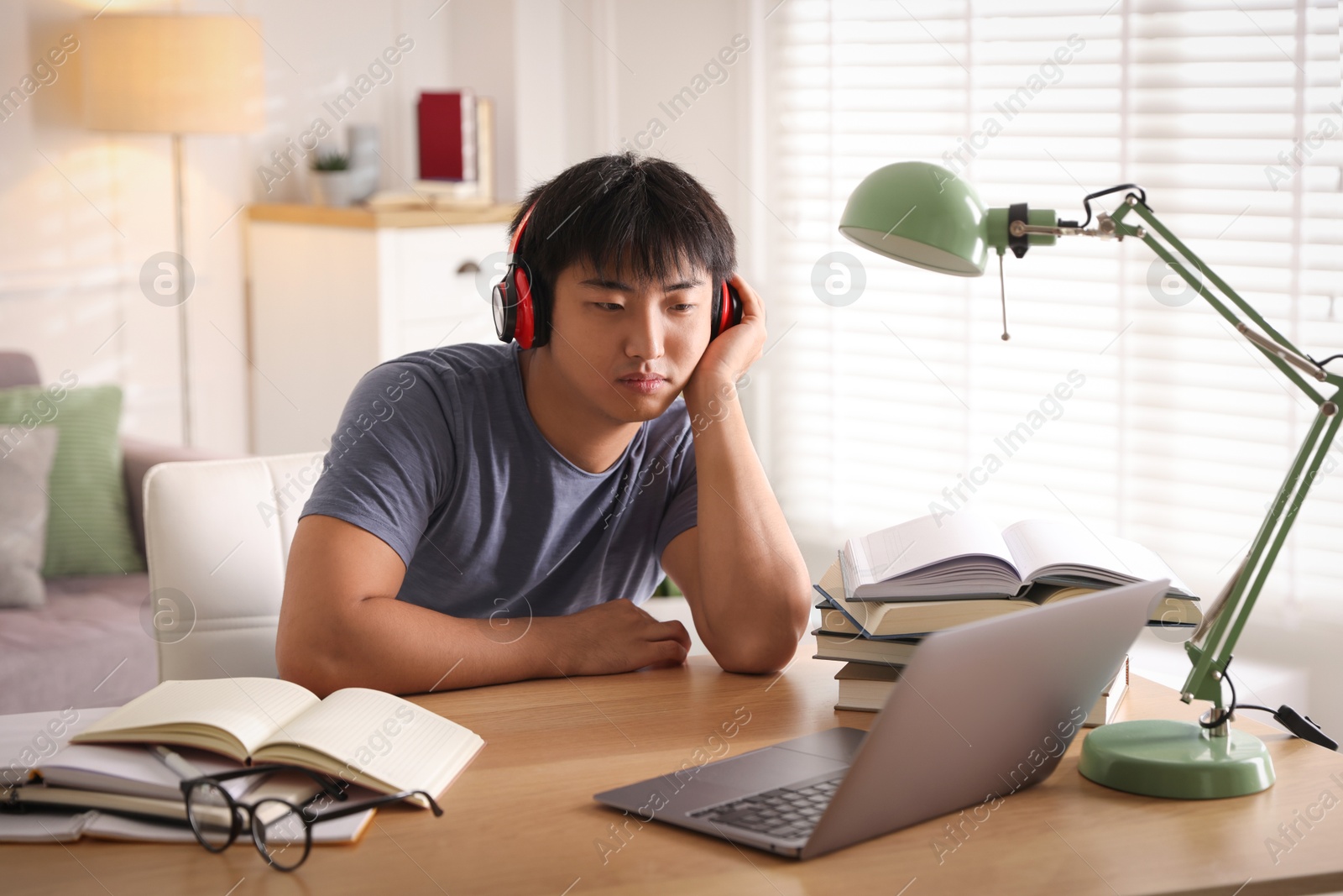 Photo of Student in headphones with laptop and books preparing for exam at table indoors