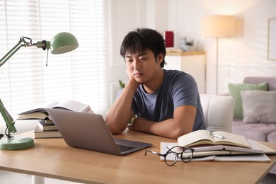 Photo of Student with laptop and books preparing for exam at table indoors