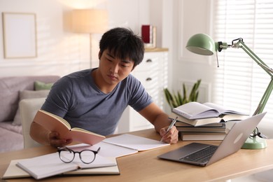 Photo of Student with laptop and books preparing for exam at table indoors