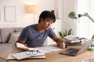 Photo of Student with laptop and books preparing for exam at table indoors