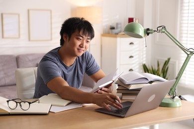 Photo of Student with laptop and books preparing for exam at table indoors