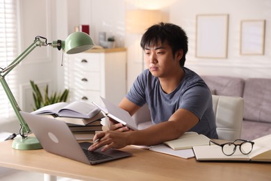 Photo of Student with laptop and books preparing for exam at table indoors