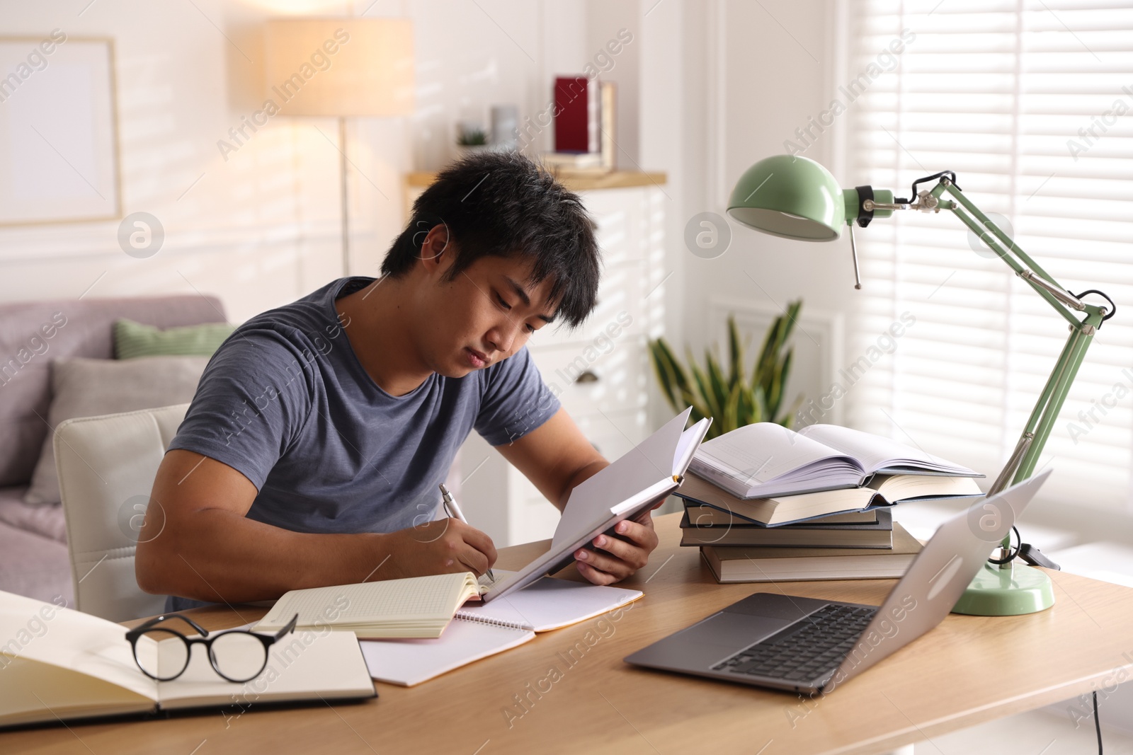 Photo of Student with laptop and books preparing for exam at table indoors