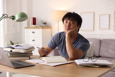 Photo of Student with laptop and books preparing for exam at table indoors