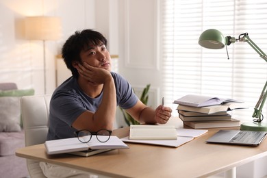 Photo of Student with laptop and books preparing for exam at table indoors