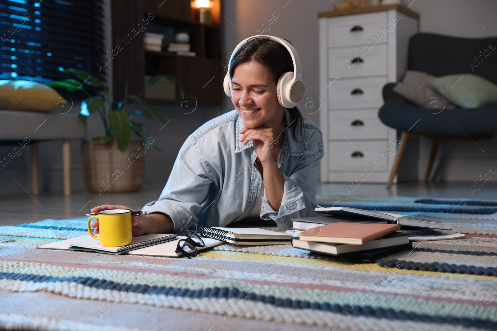 Photo of Happy student in headphones preparing for exam on floor at home