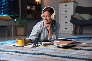 Photo of Happy student in headphones preparing for exam on floor at home