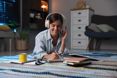 Photo of Happy student in headphones preparing for exam on floor at home