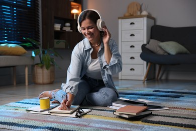 Photo of Happy student in headphones preparing for exam on floor at home