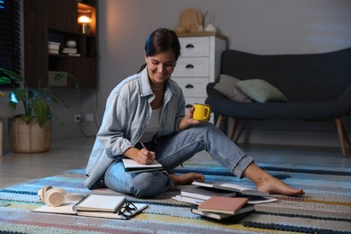 Photo of Happy student with cup of drink preparing for exam on floor at home