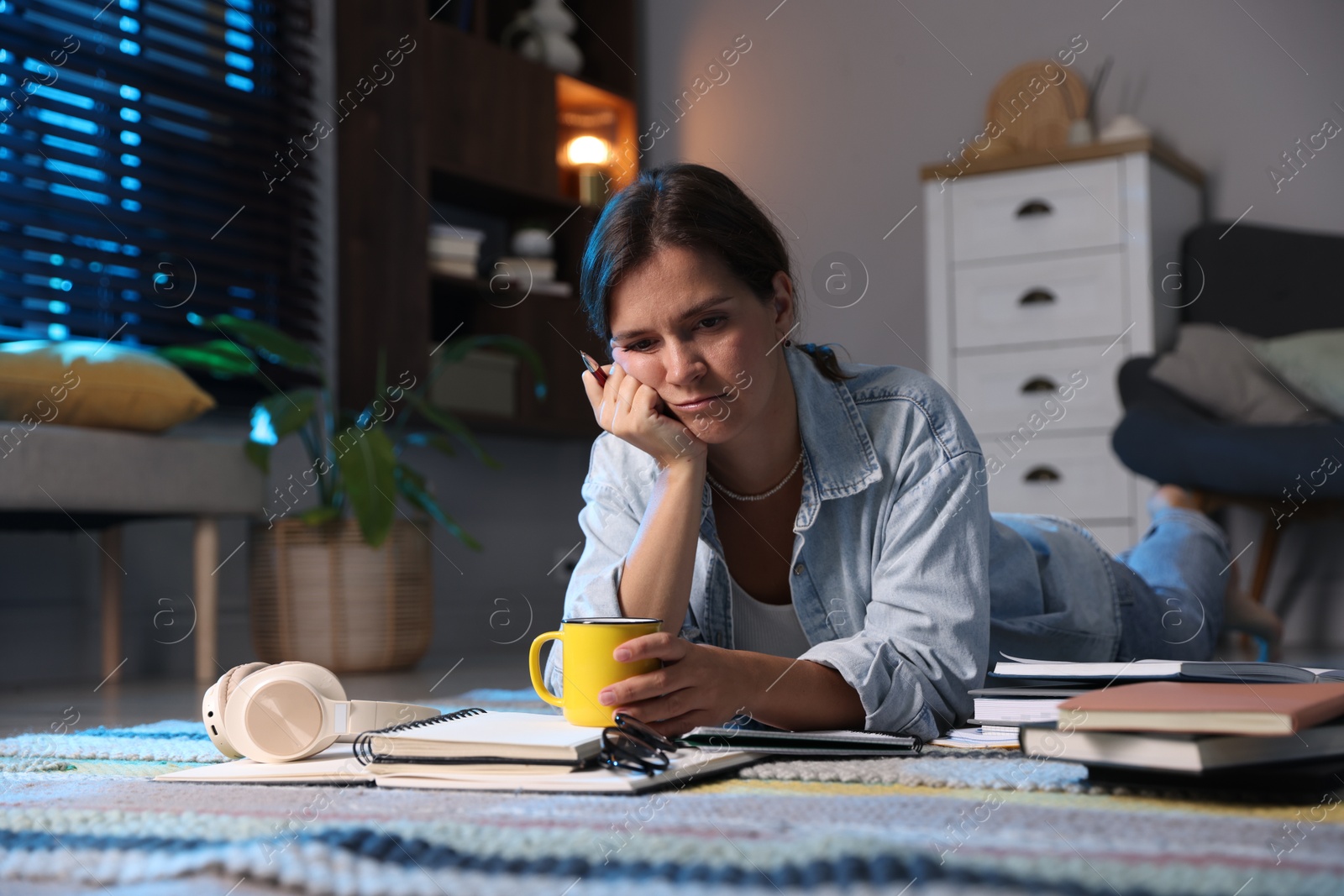 Photo of Tired student with cup of drink preparing for exam on floor at home